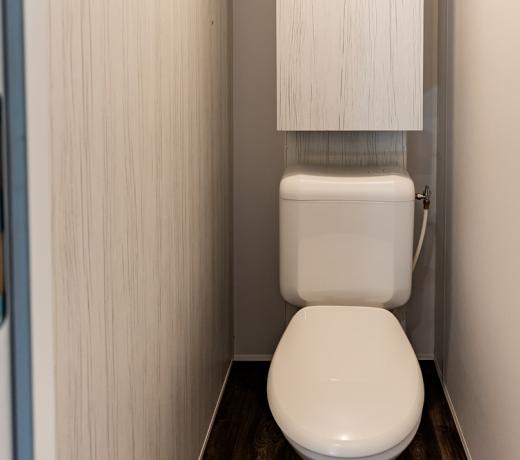 Stretto bagno con WC e serbatoio sopraelevato, pareti chiare.