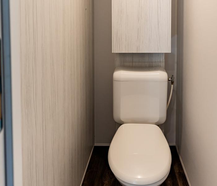 Stretto bagno con WC e serbatoio sopraelevato, pareti chiare.